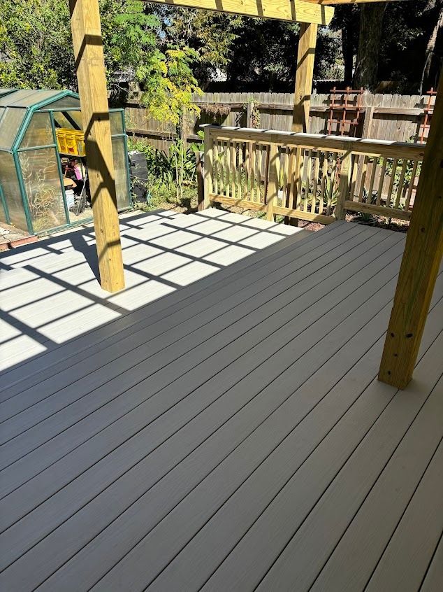Wooden deck with shadows cast by a pergola. A small greenhouse is to the left.