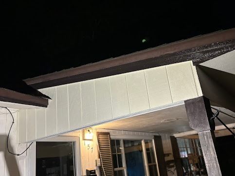 View from below of a building's exterior at night; cream siding, dark wood trim, night sky with a glowing orb.