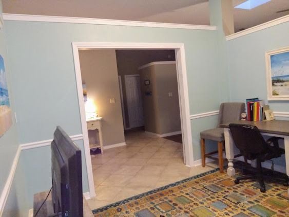 Room with light blue walls, a doorway leading to a hallway, a desk, and a rug.