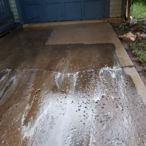 Wet concrete driveway in front of a blue garage door, with cleaning agent residue.