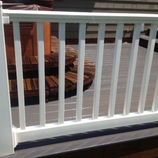 White railing on a wooden deck, with a circular staircase and hot tub visible in the background.