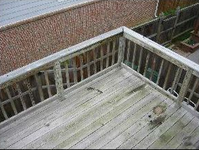 Wooden deck with weathered planks, railings, and brick wall in the background.