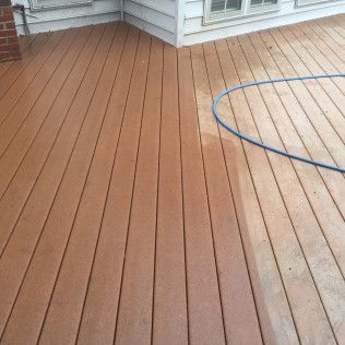 Wooden deck being cleaned with a hose; the cleaned area is lighter than the rest.