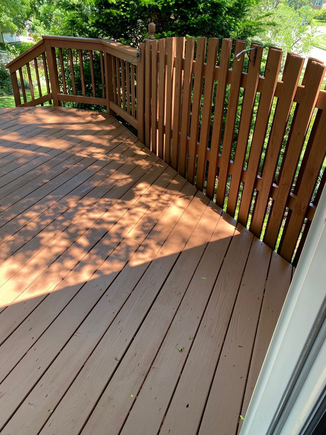 Wooden deck with brown railing and gate in a sunny outdoor setting.