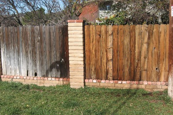 Wooden fence with brick accents; weathered wood next to newer-looking wood. Green grass and blue sky in the background.