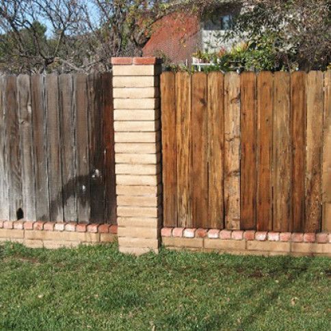 Weathered wooden fence, brick pillar and base, dividing fence section with new wood. Green grass.
