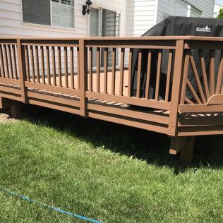 Brown wooden deck with railing in backyard, grass in foreground, grill covered on deck.