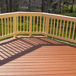 Wooden deck with tan railing casting shadows on the reddish-brown planks.