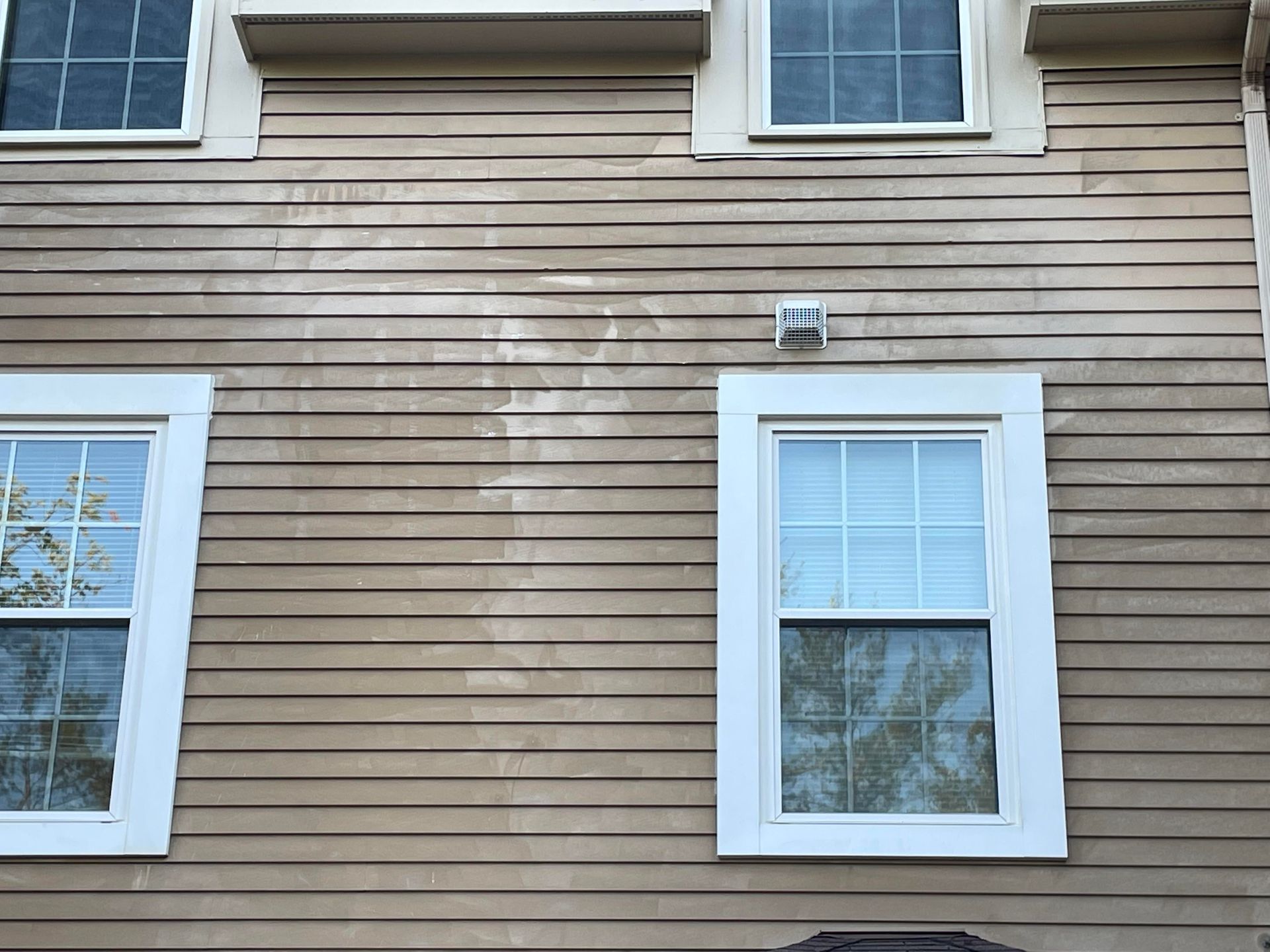 Beige siding of a building with three white-framed windows, and an air vent.