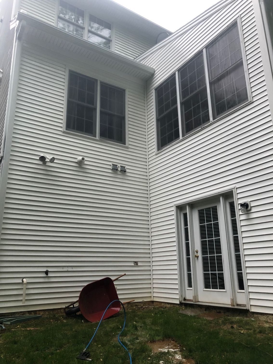 White house exterior with windows and a door, a wheelbarrow, and grass.