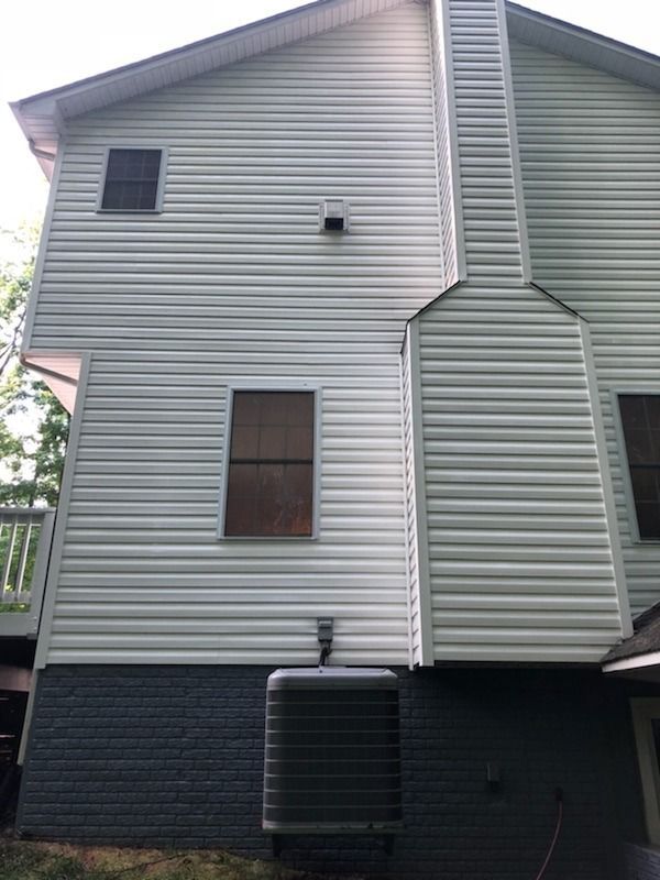 Side of a house with white siding, chimney, and air conditioner. Dark gray brick base.