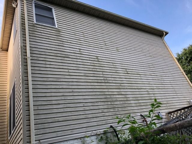 Beige siding of a two-story house with visible streaks of dirt and grime on a sunny day.