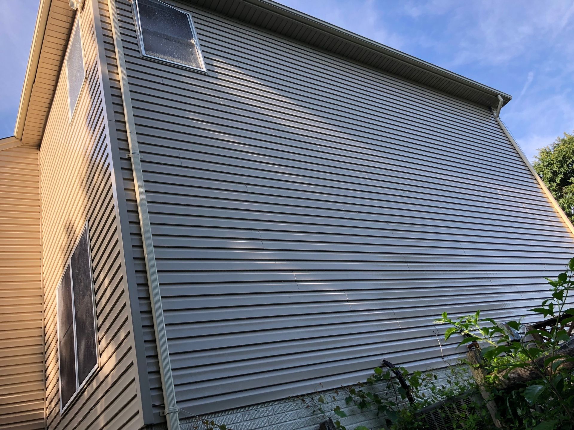 Side view of a two-story house with beige and grey siding under a blue sky.
