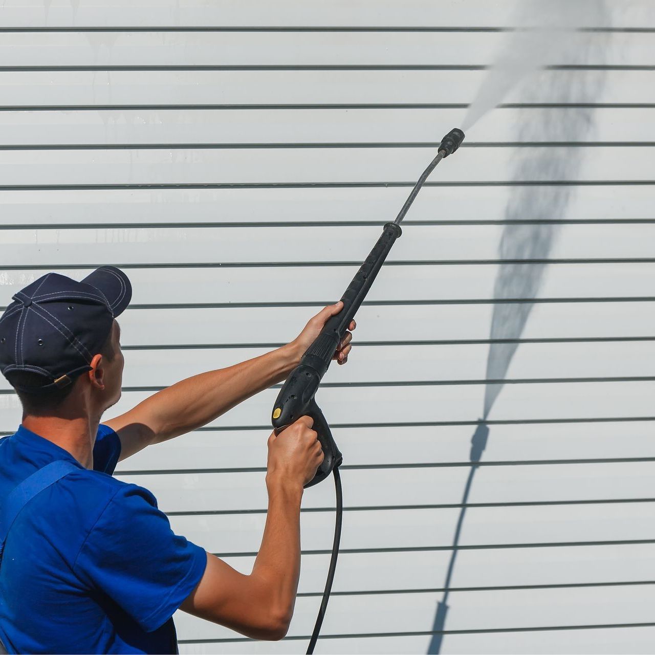 worker-overalls-washes-white-wall-from-siding-with-water-gun