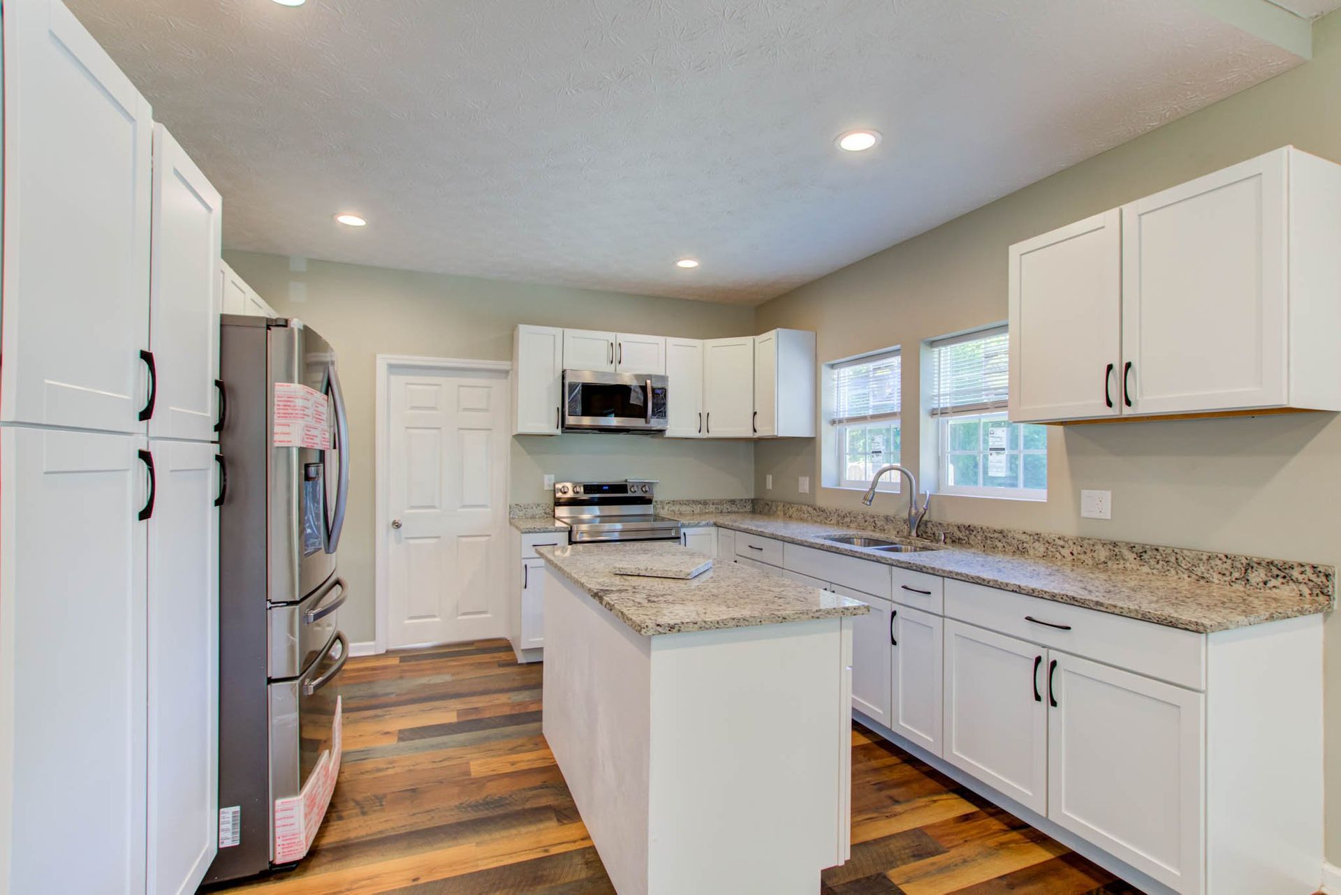 A kitchen with white cabinets , granite counter tops , stainless steel appliances and a large island .