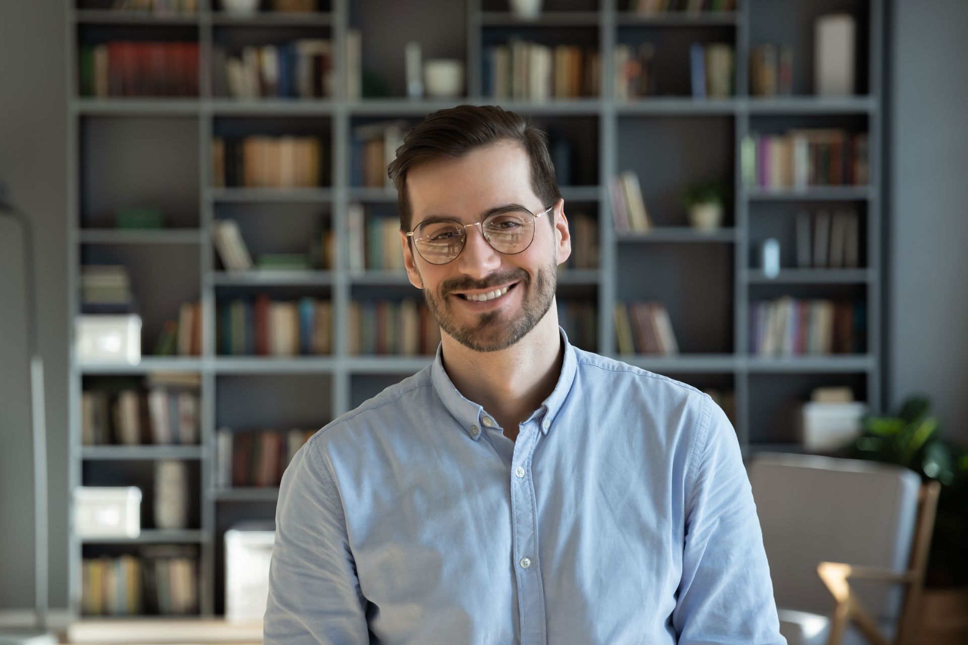 A man wearing glasses is smiling in front of a bookshelf .