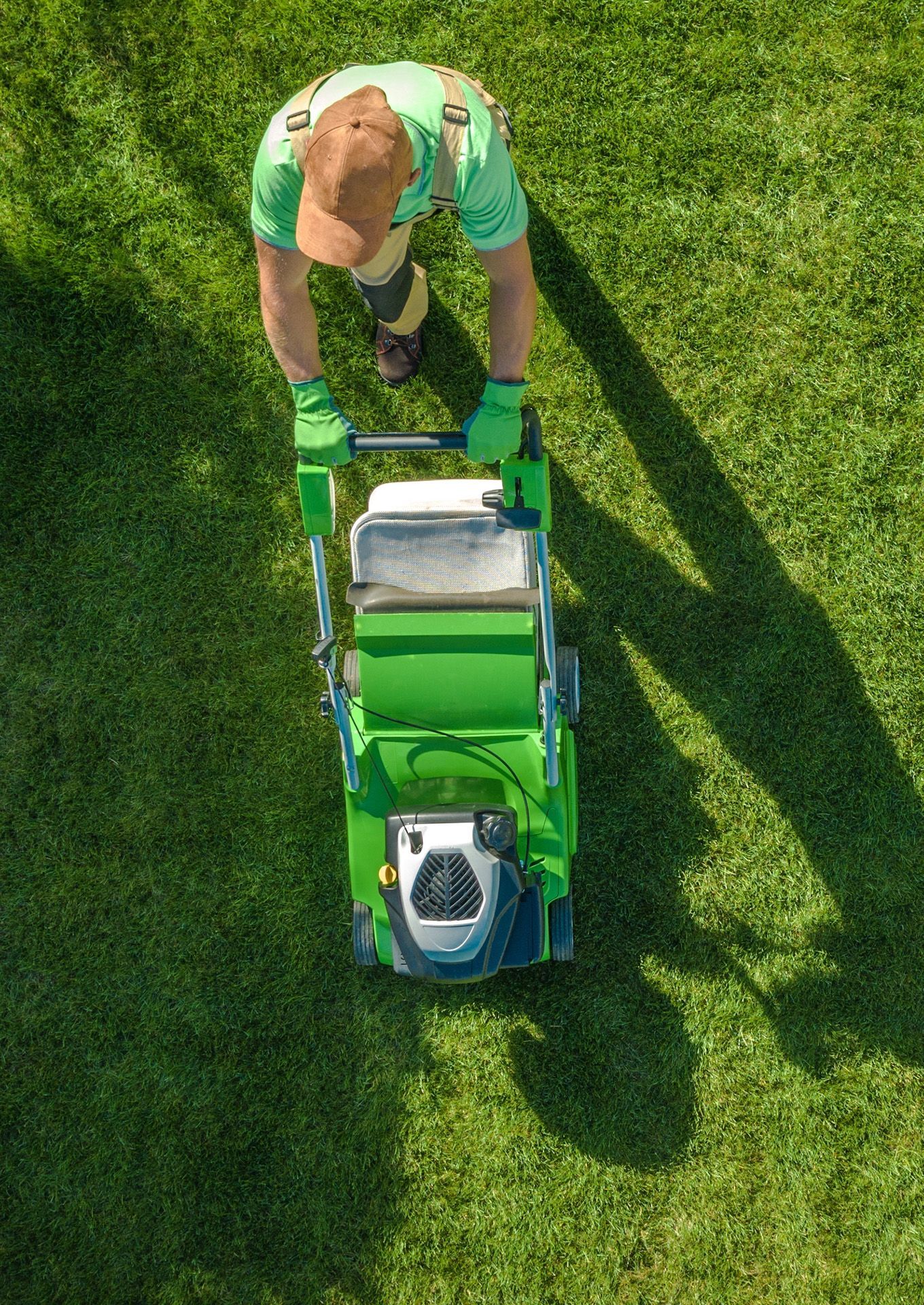 A man is cutting the grass with a green lawn mower.