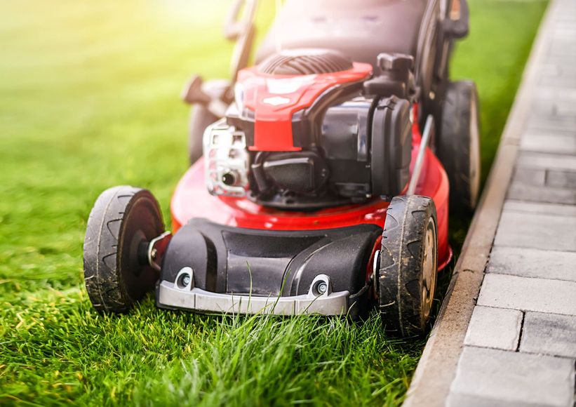 A red lawn mower is cutting a lush green lawn.