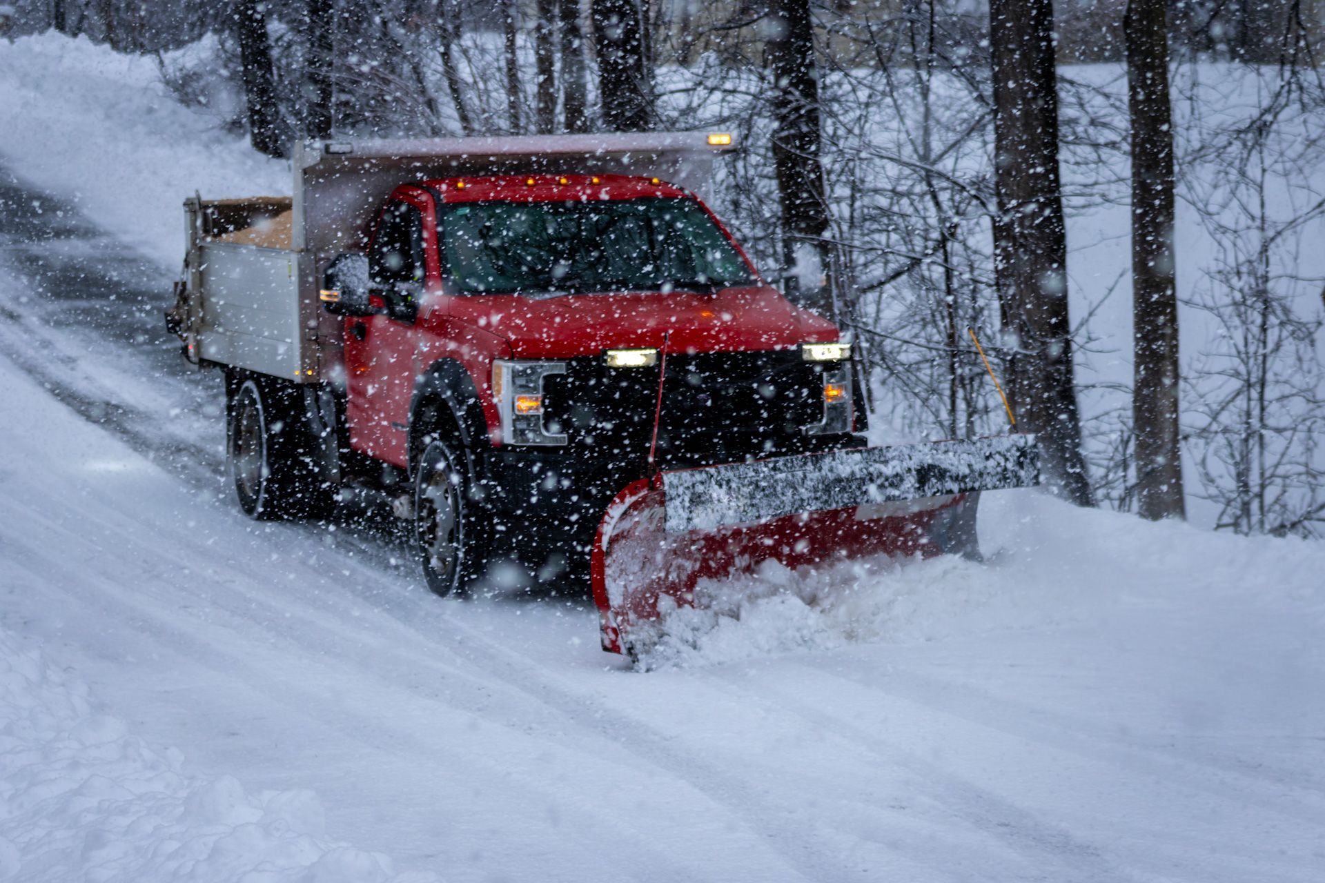 A red truck is plowing snow on a snowy road.