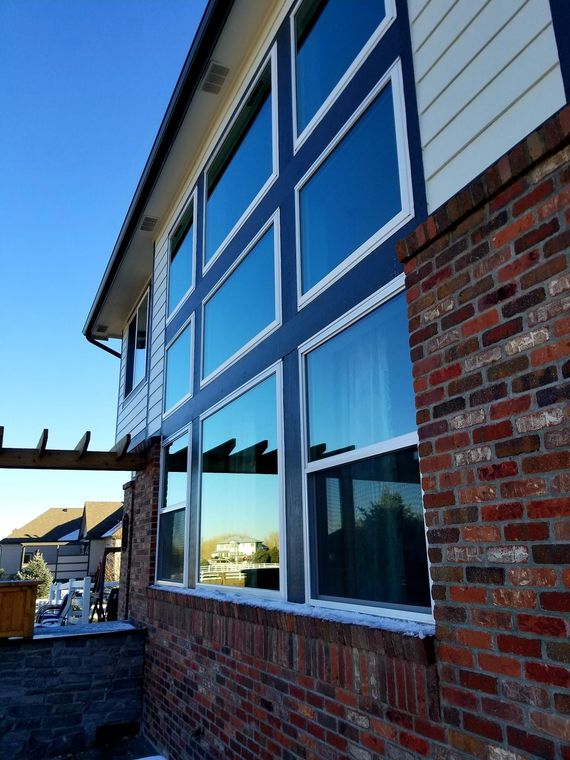 Exterior of a brick house with large blue-trimmed windows reflecting a sunny street.