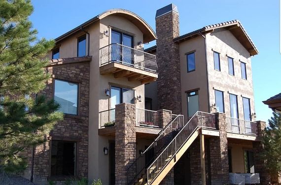 Modern multi-story apartment building with balconies, stone exterior, and outdoor stairs under a blue sky
