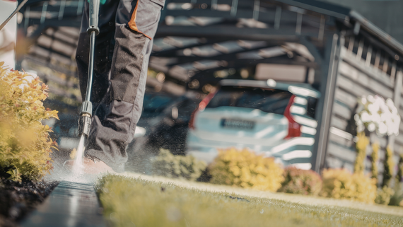 A person power-washing a sidewalk near a bridge, with water spraying across the pavement.