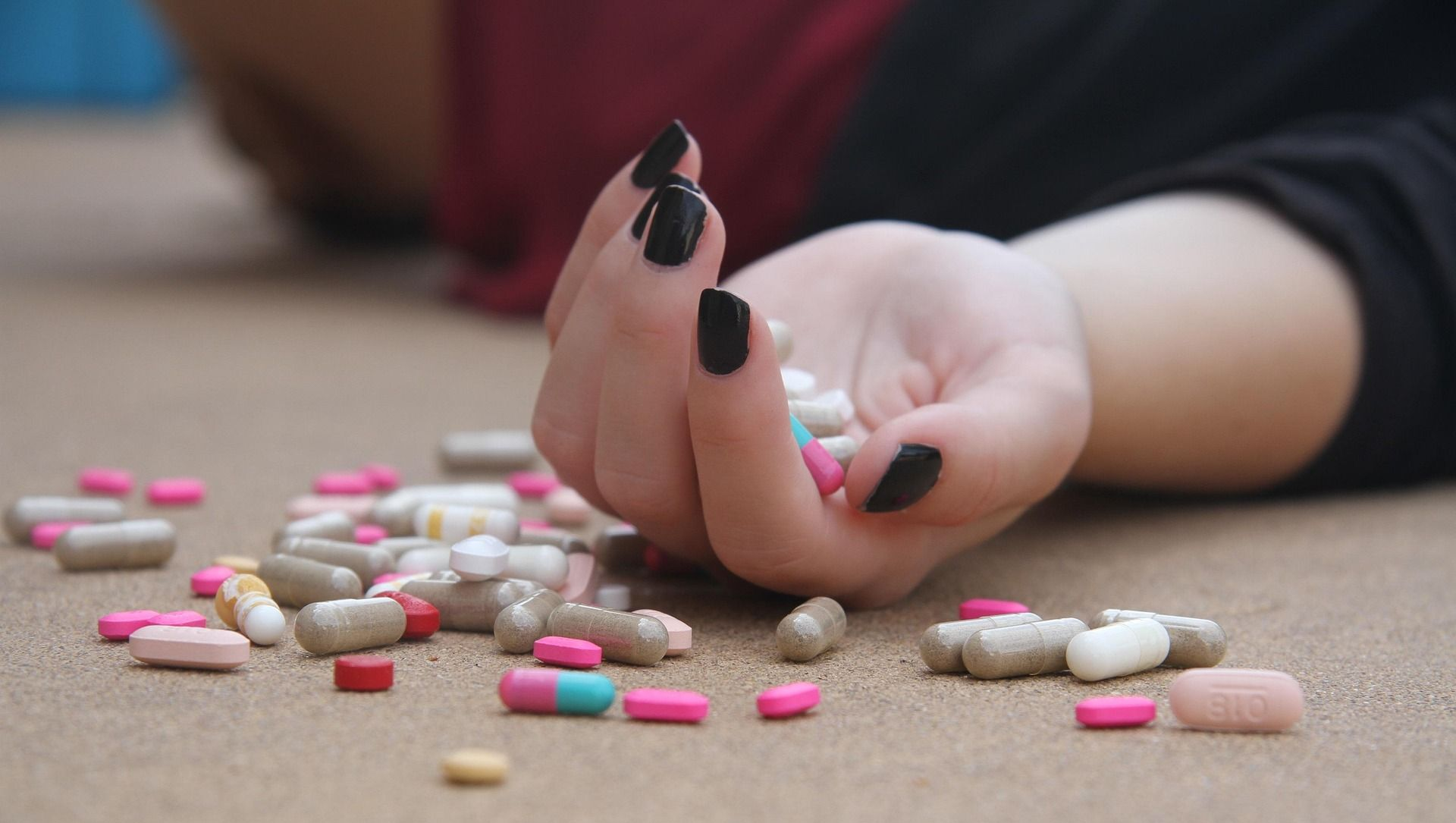 Hand reaching toward scattered pills on the floor, suggesting a possible overdose or drug misuse