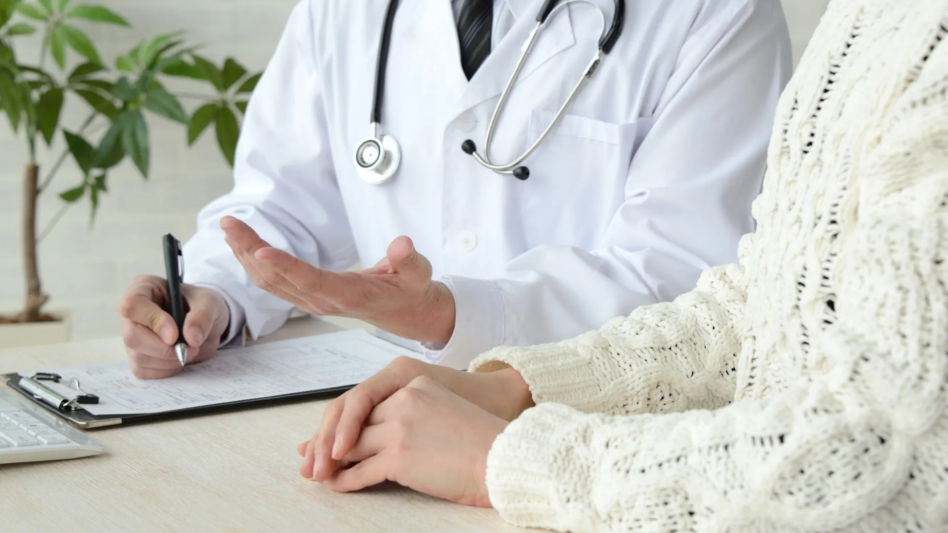 Doctor consulting with a patient, taking notes on a clipboard in a bright clinic office.