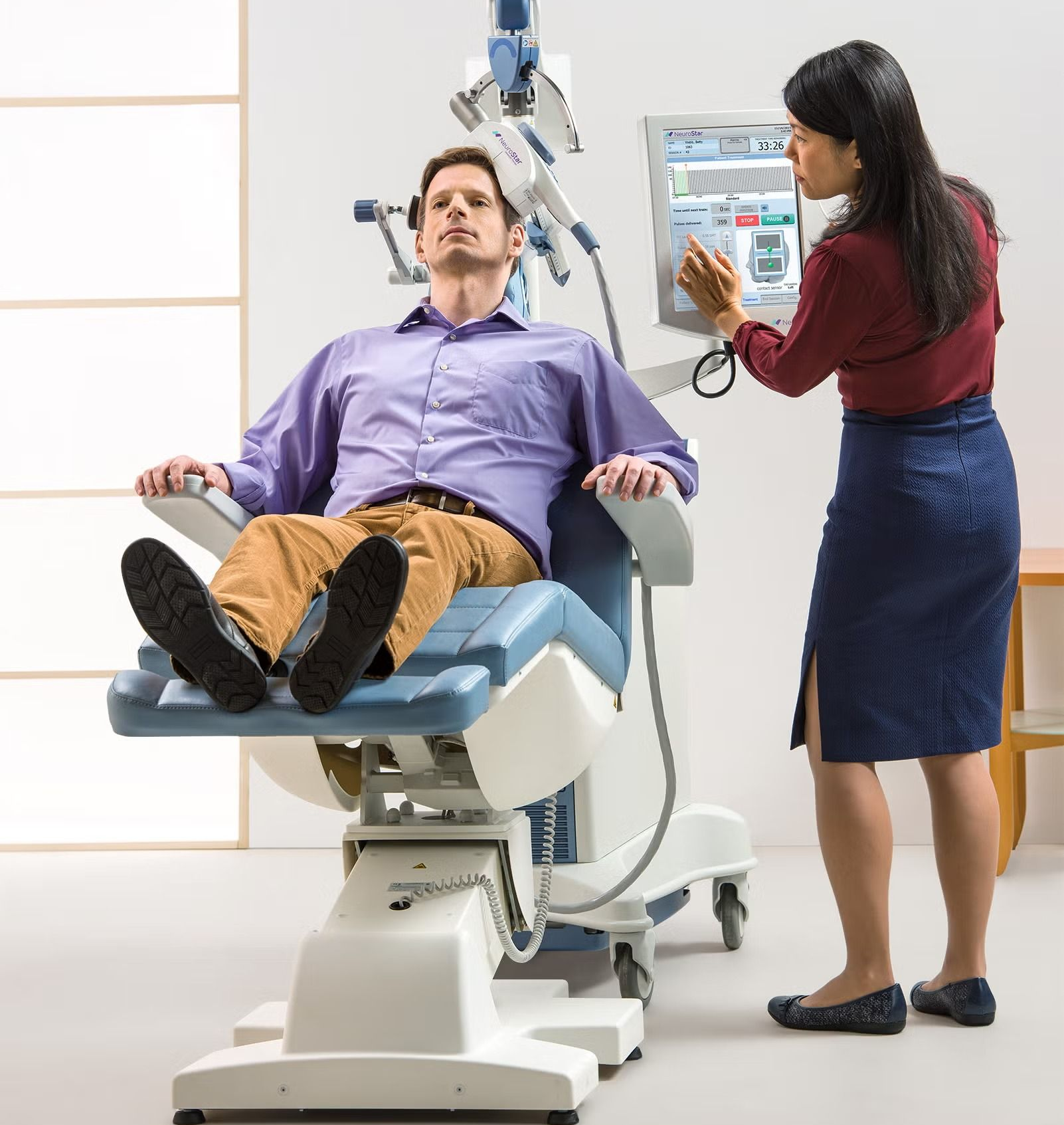 Patient on a medical exam chair while a clinician adjusts a device on a control panel.
