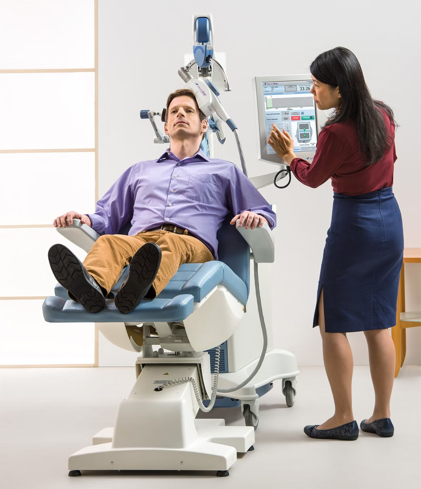 Patient reclines in a dental chair while a clinician gestures at a monitor beside him.