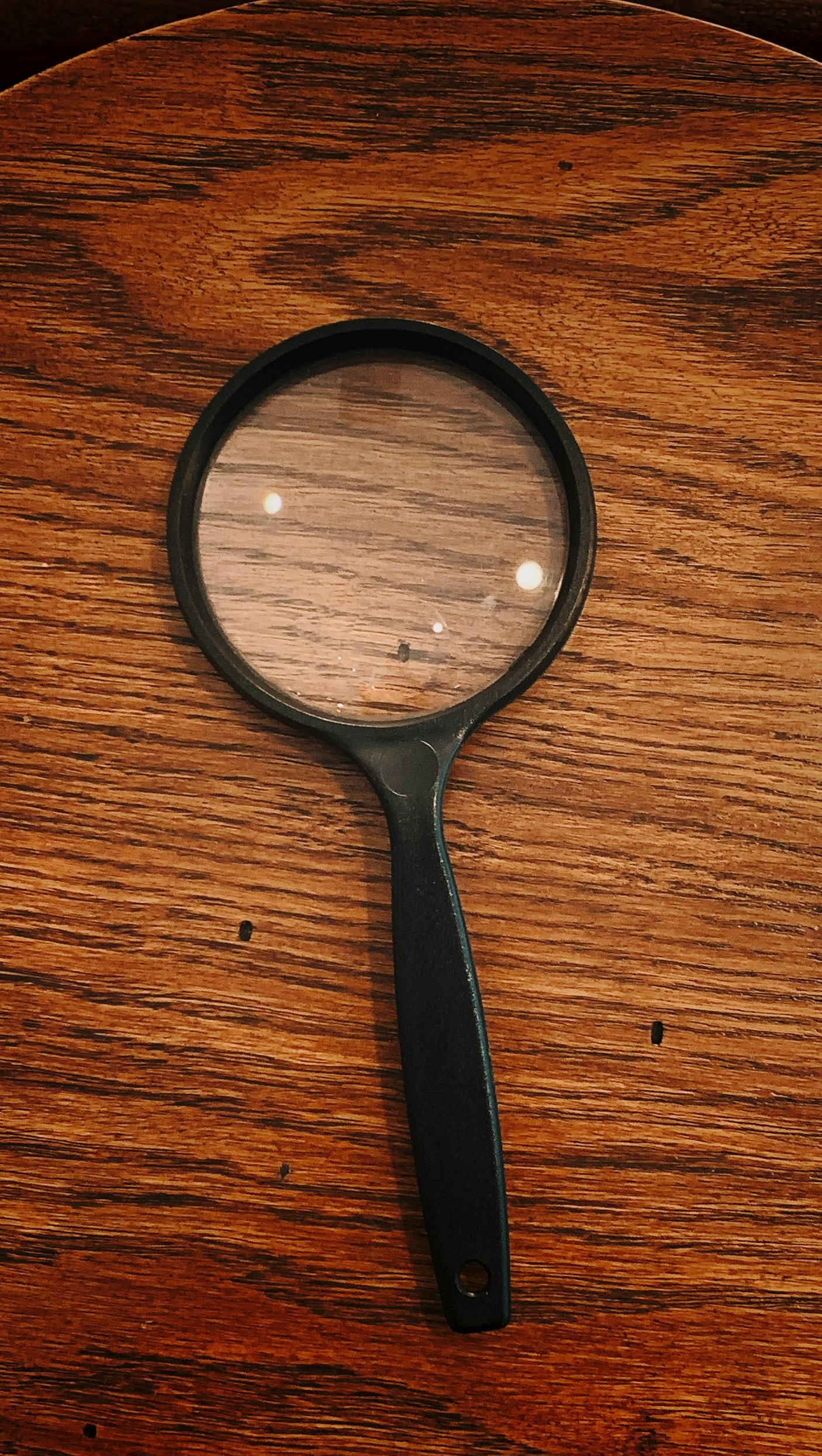 Black-handled magnifying glass on a wooden surface.