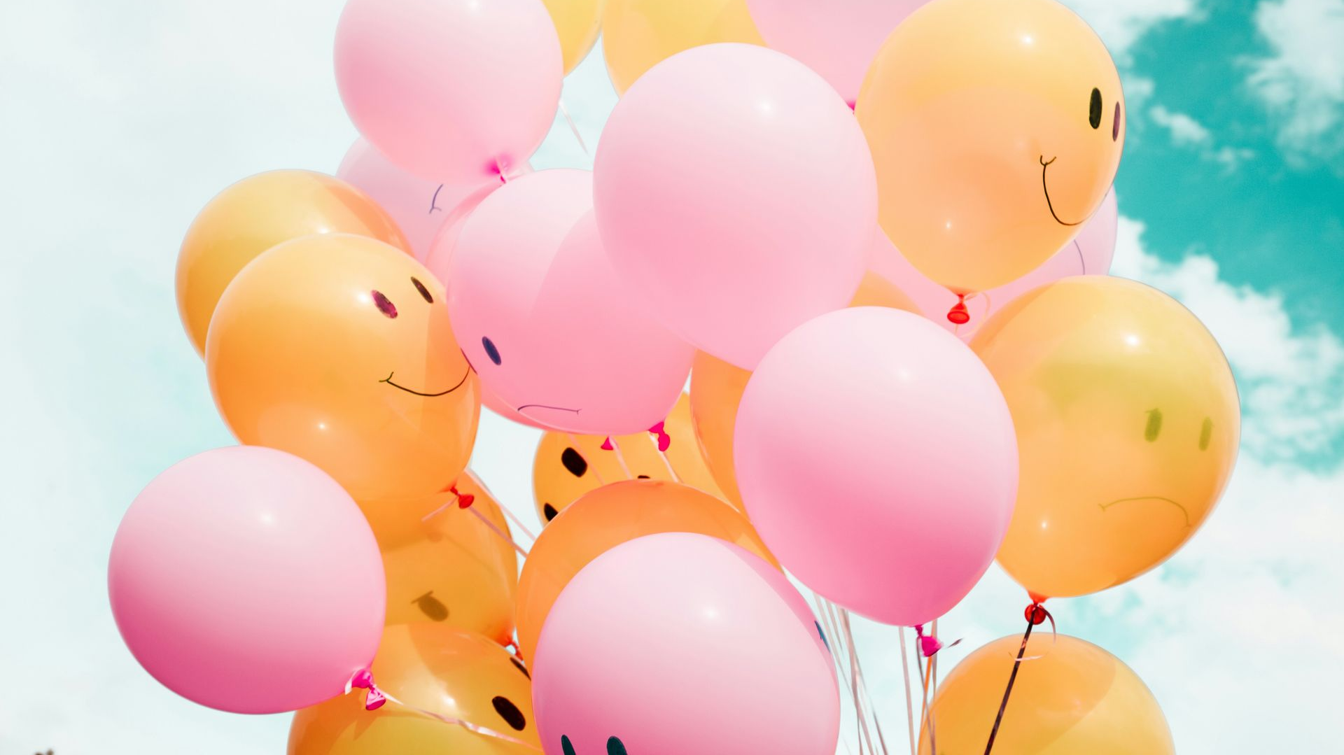 Pink and yellow balloons floating against a blue sky with clouds