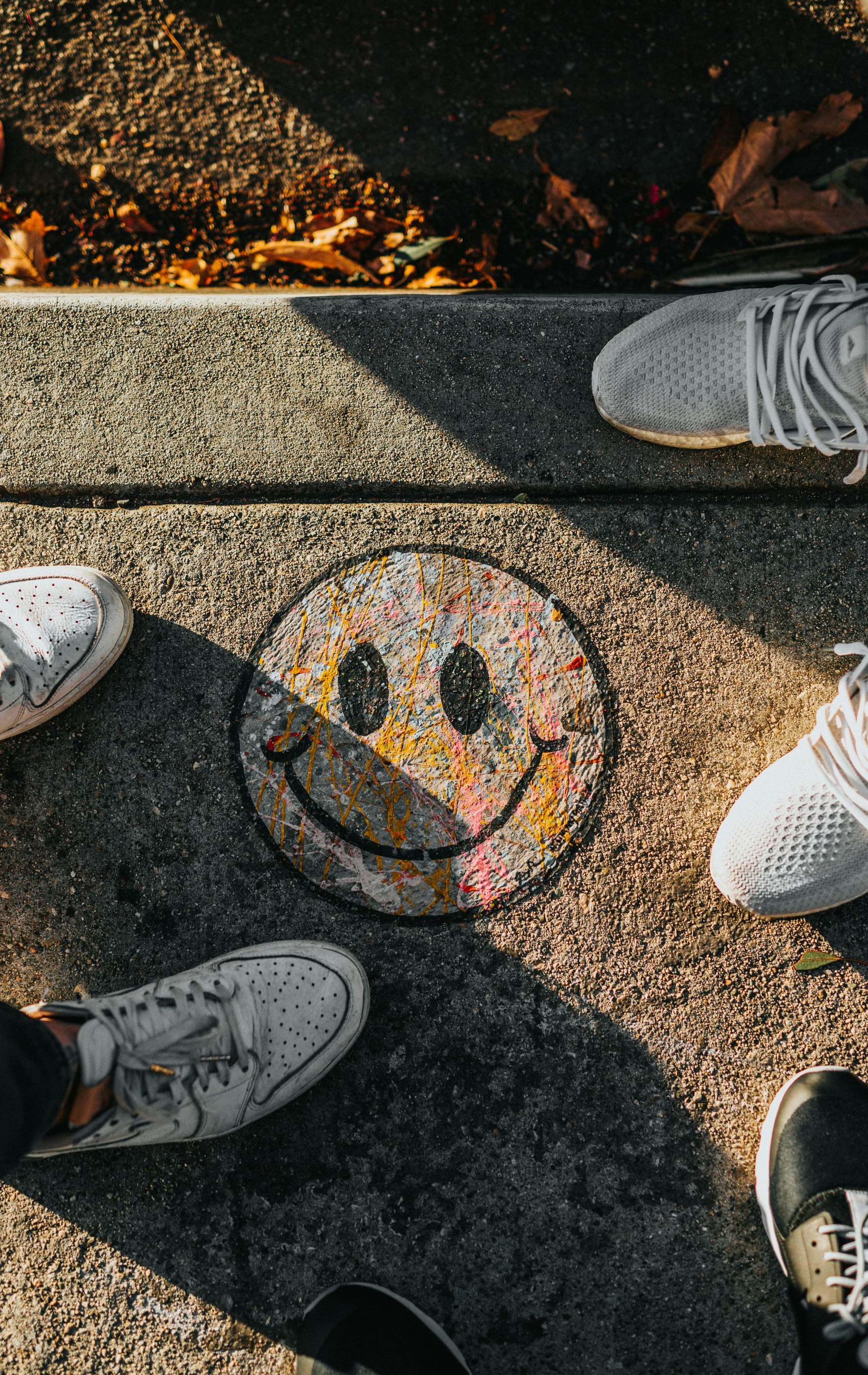 Smiley face chalk drawing on pavement, surrounded by several sneakers in a sunlit outdoor area