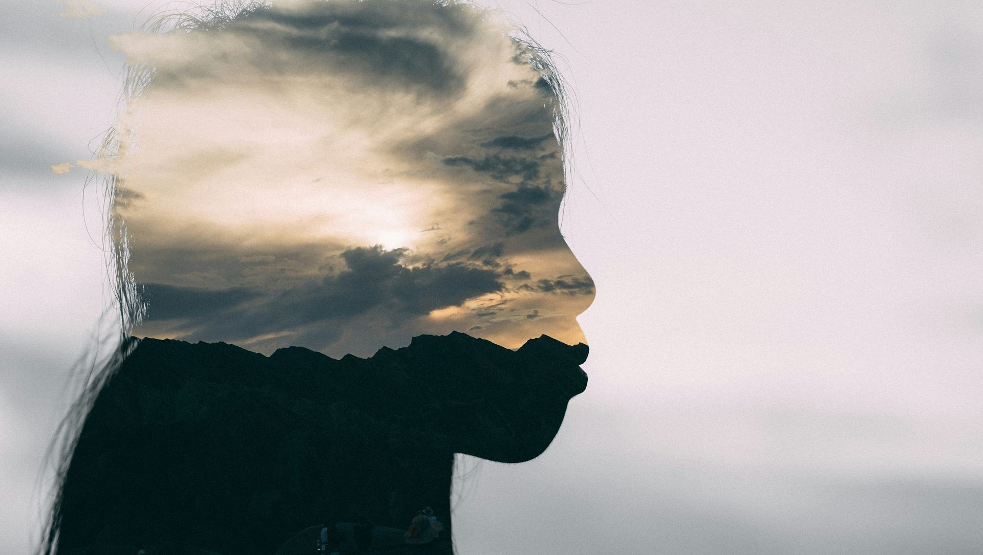 Silhouette of a person overlaid with a cloudy sunset sky against a pale background