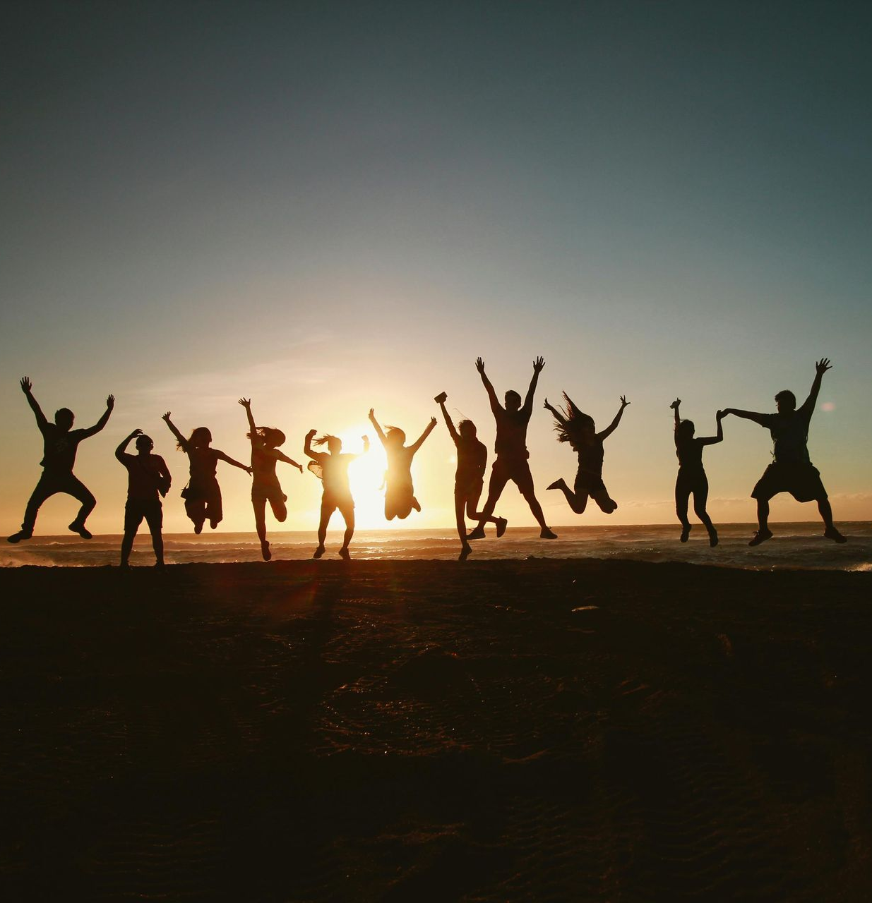 Silhouetted people jumping on a beach at sunset with the sun low on the horizon