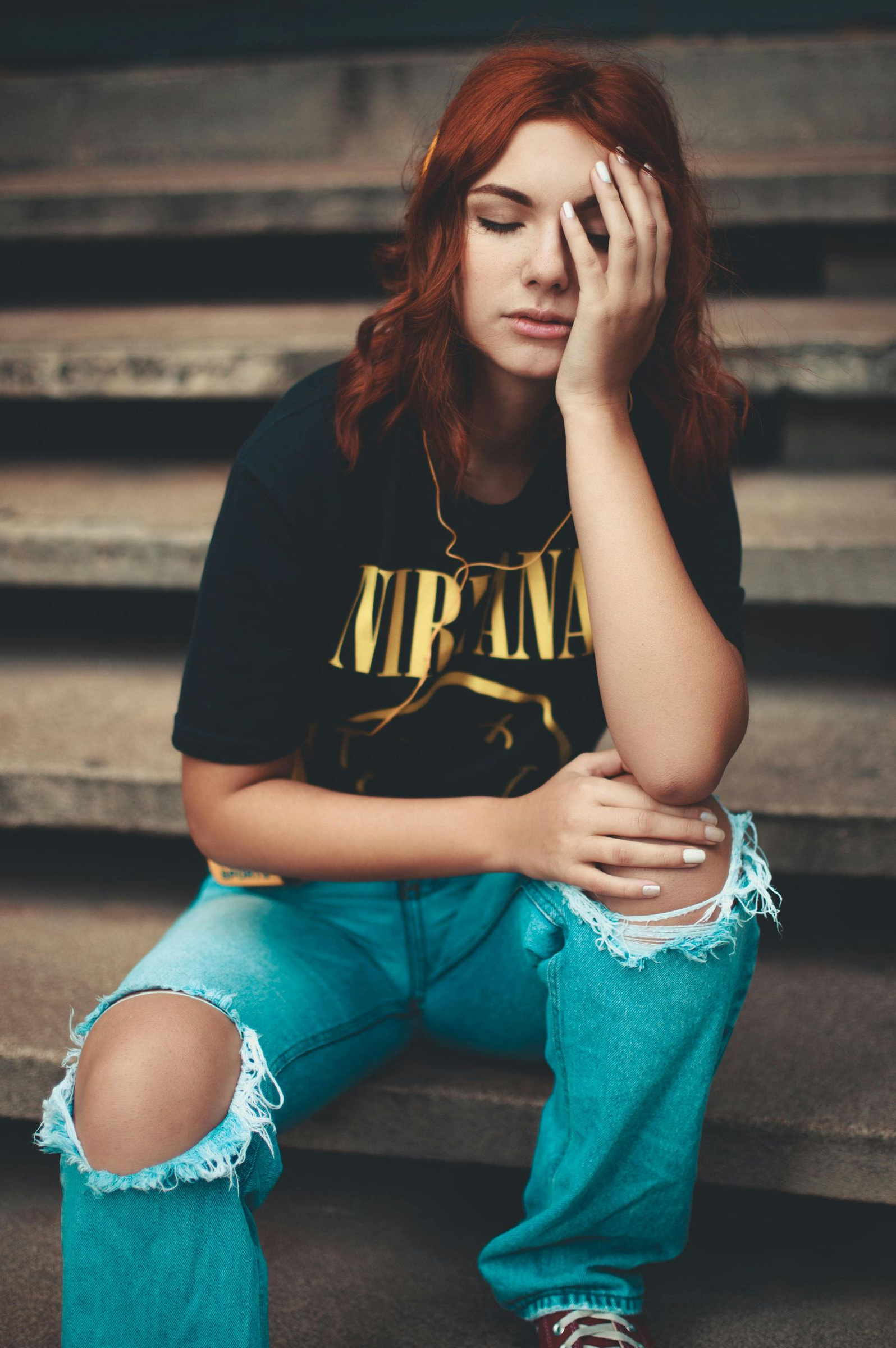Seated person in a black shirt and teal jeans on steps, resting head on one hand