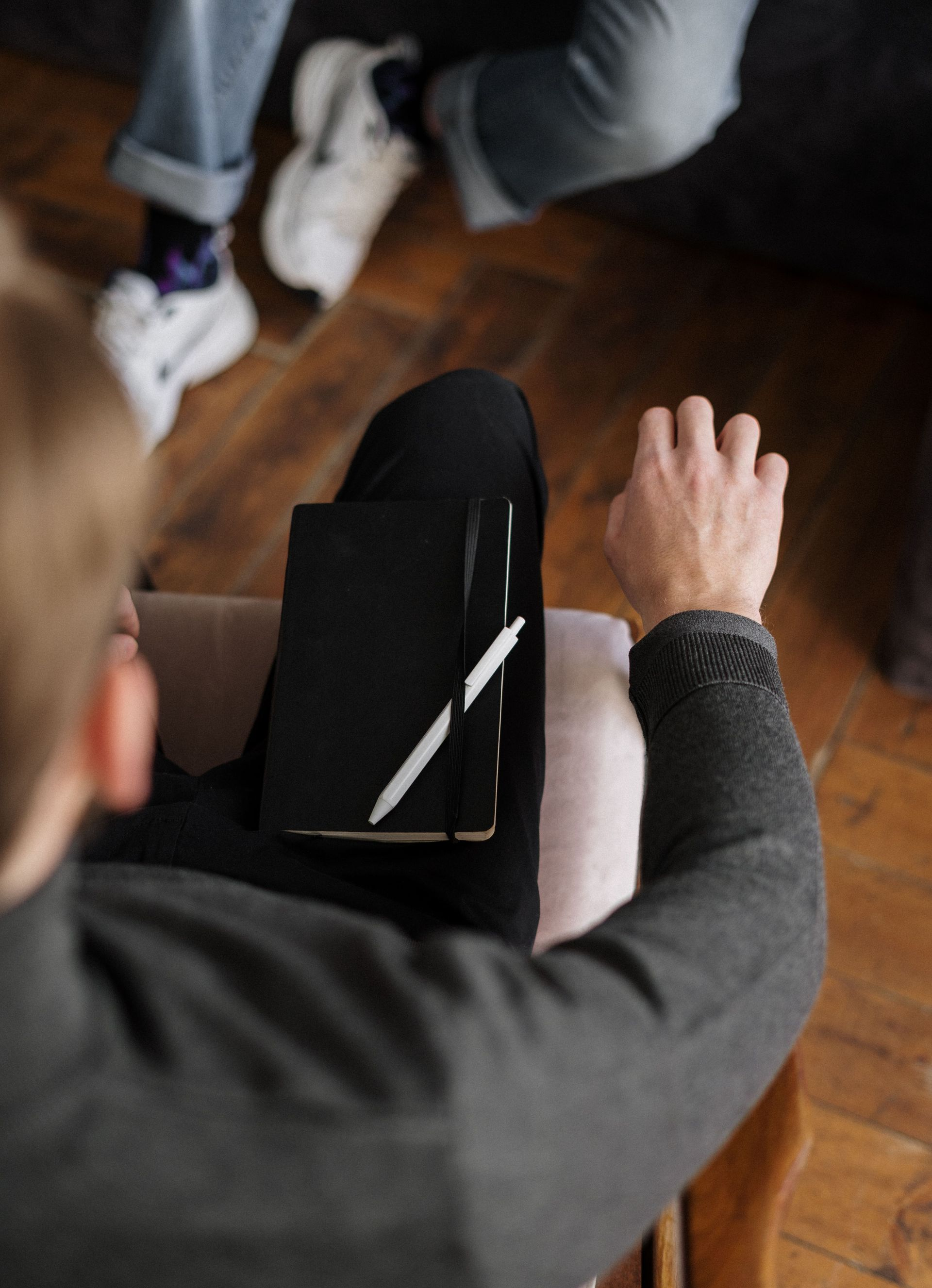 Person seated with a black tablet on their lap, reaching a hand forward in a room with a wooden floor.