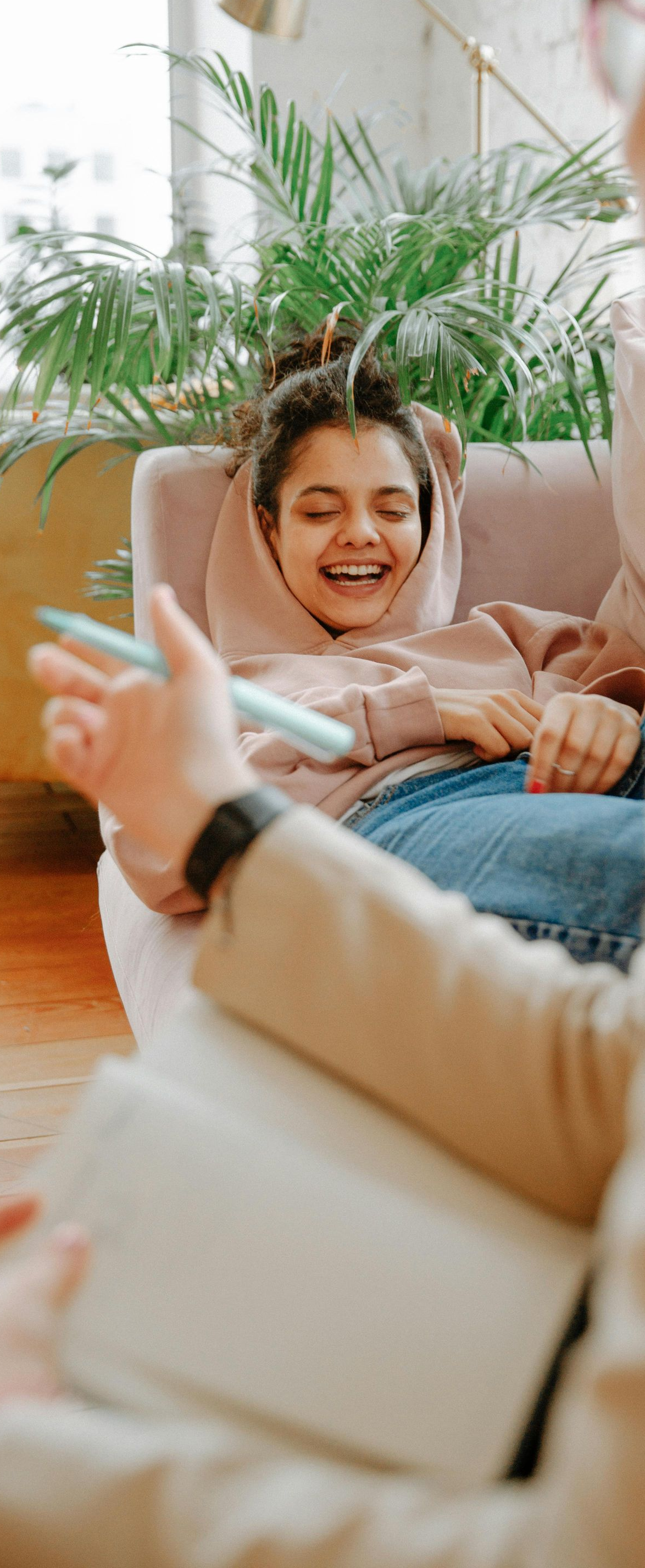 Person smiling on a couch, holding a phone, with plants in the background