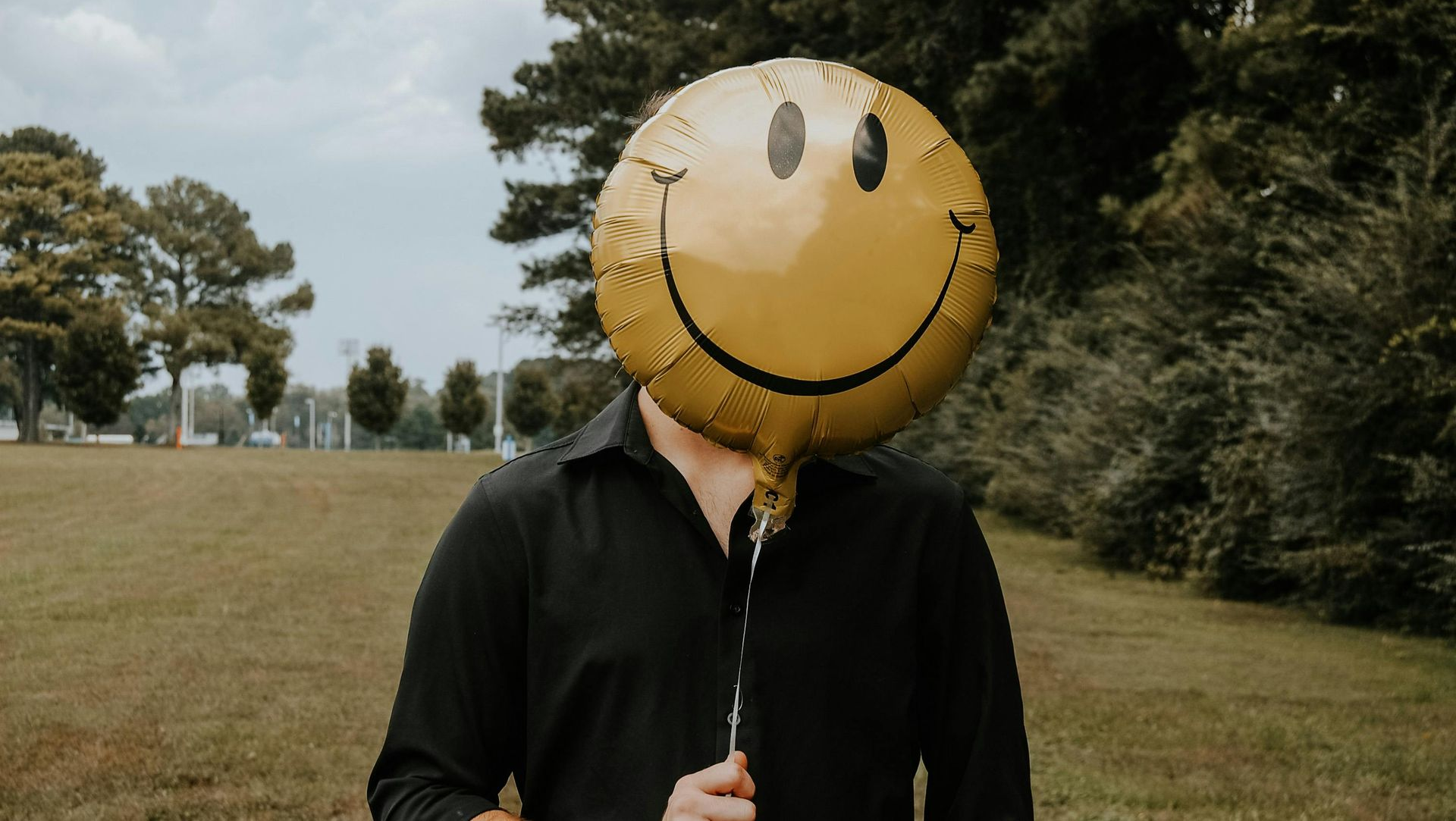 Person holding a yellow smiley-face balloon in a grassy park
