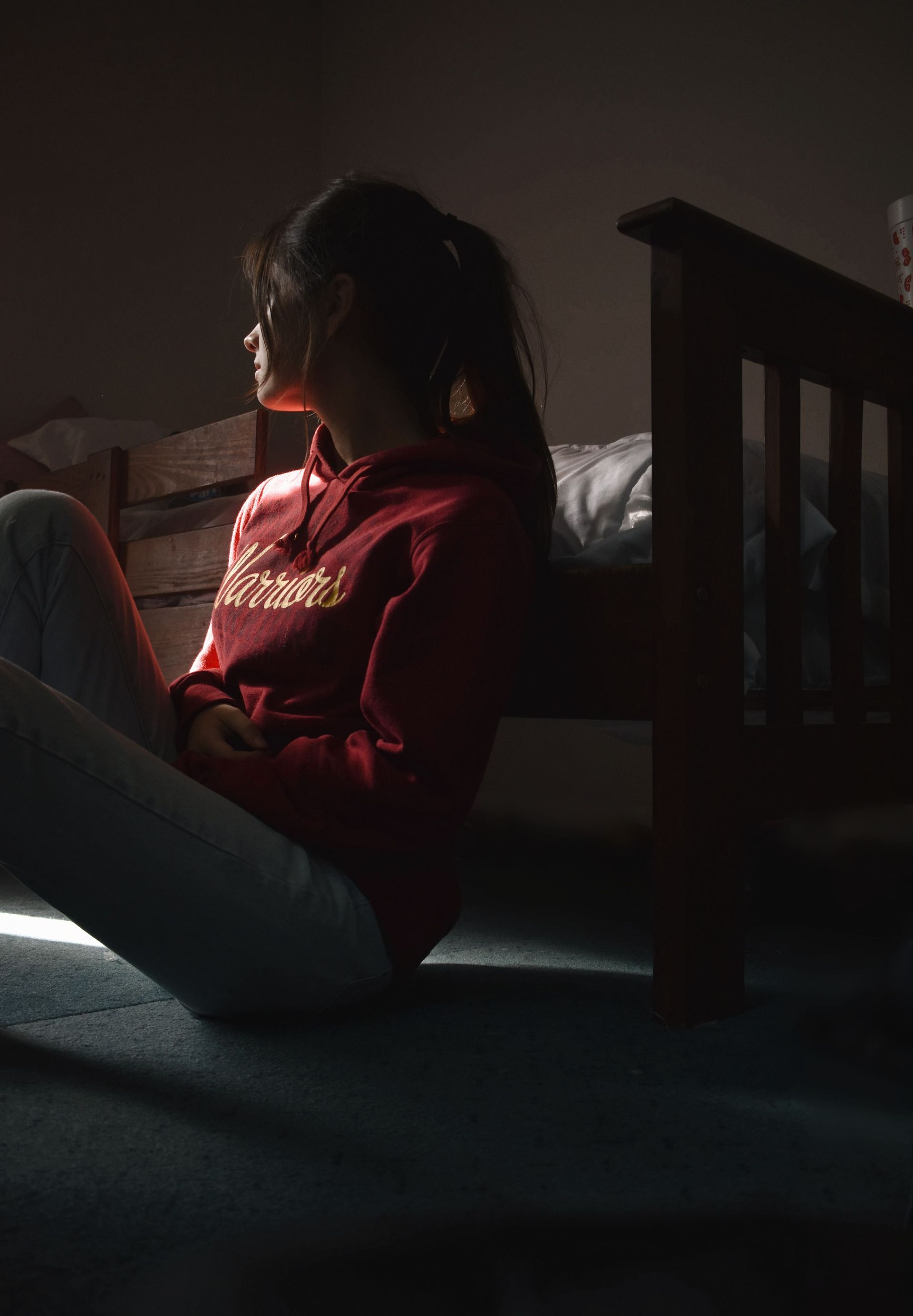 Person in a red sweater sitting on the floor by a staircase, lit by soft window light.