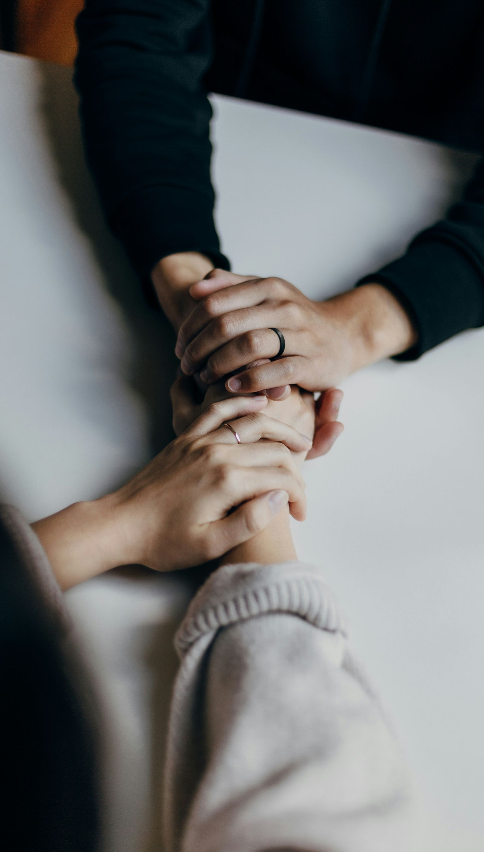 Hands stacked together in a circle, showing teamwork and support on a light surface.