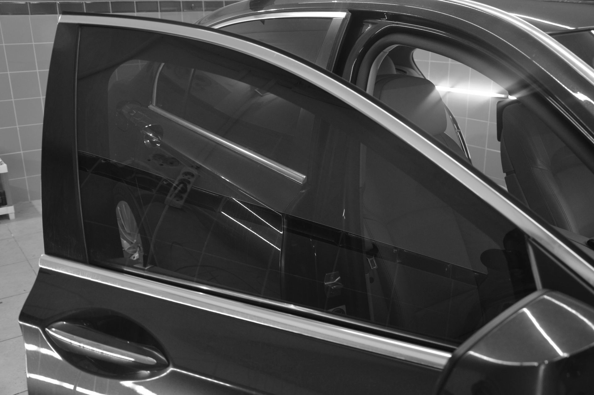 Black car with a tinted side window and visible front mirror, parked indoors.