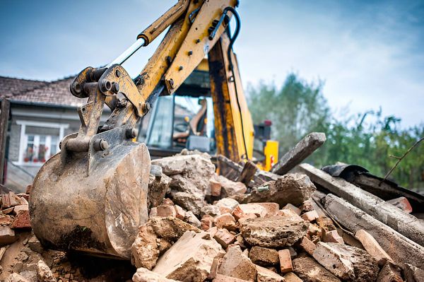 A bulldozer is demolishing a building with a pile of rocks in the foreground.