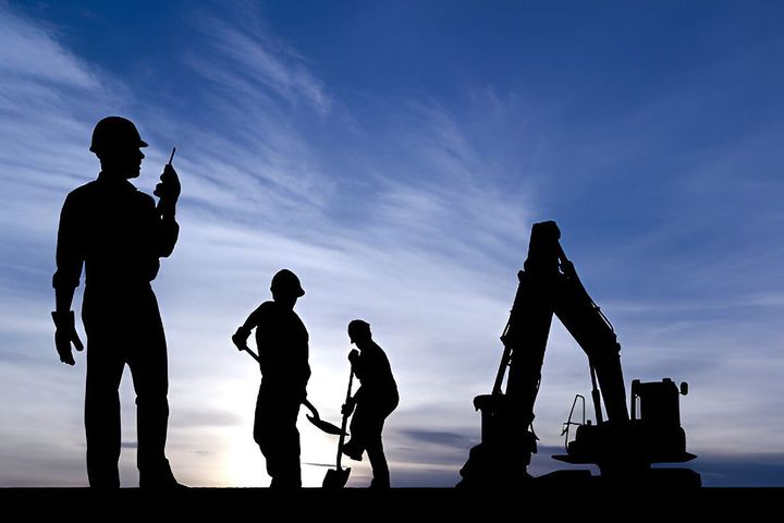 A group of construction workers are silhouetted against a blue sky