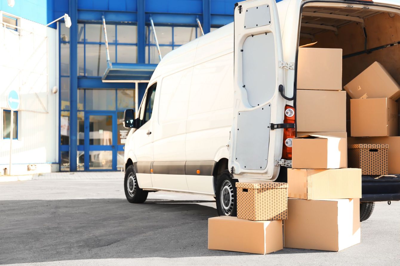 A white van is loaded with cardboard boxes in front of a building.