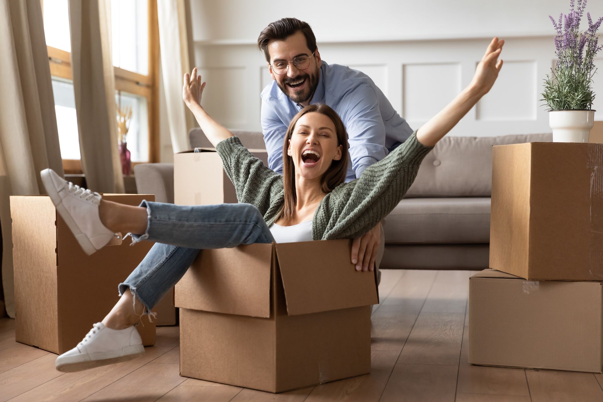 A man and a woman are sitting in cardboard boxes in a living room.