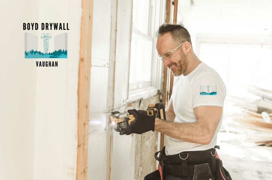 A drywall repair company professional wearing safety glasses and a white t-shirt uses an oscillating multi-tool on a wall frame at a commercial construction site near Ketelbey Ct, and Walkers Line, Burlington, ON.