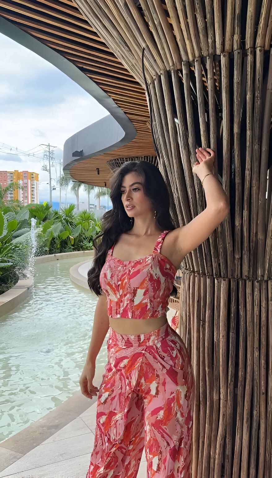Una mujer con un top y pantalones rosas está parada junto a un árbol.