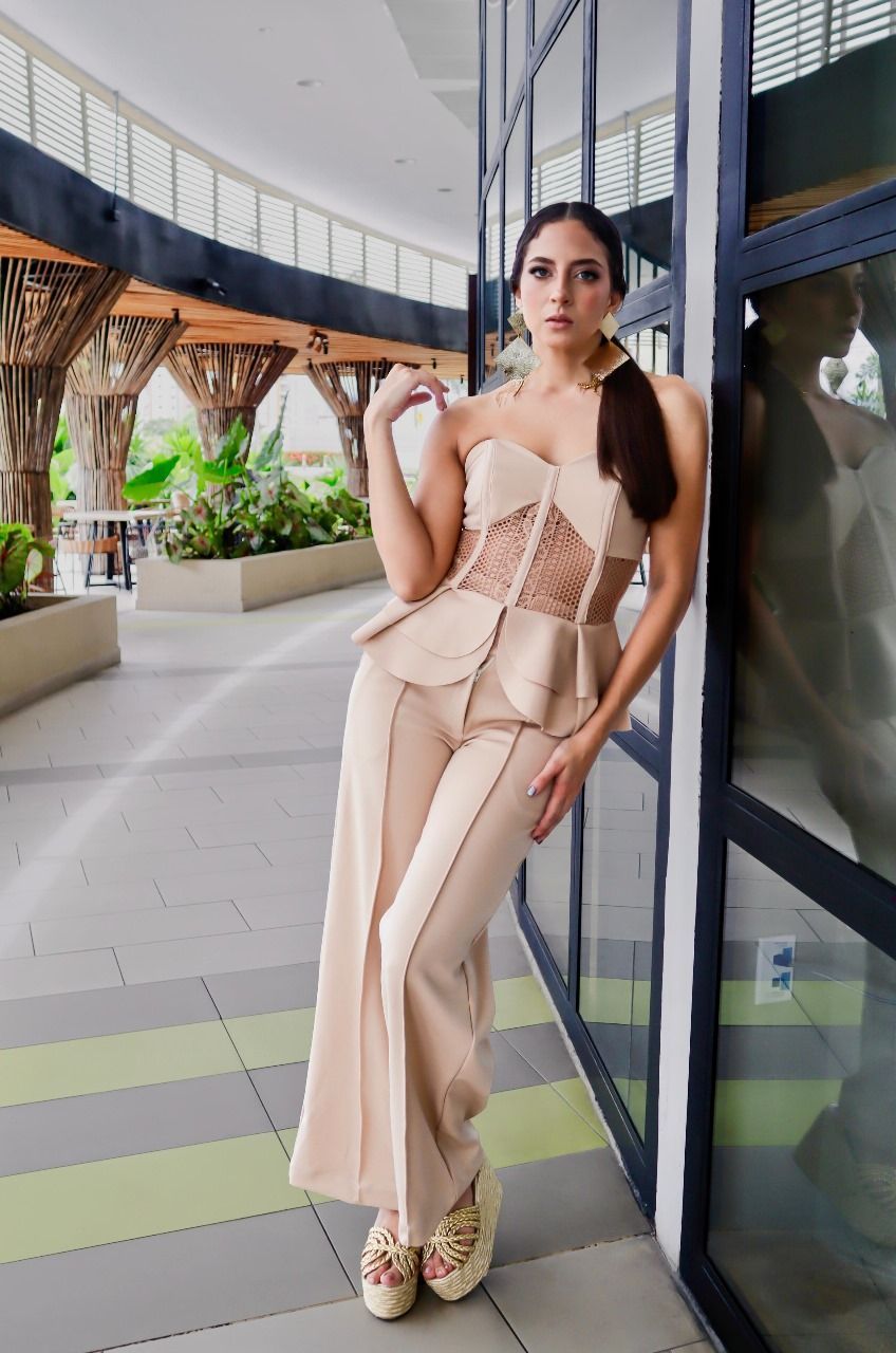 Una mujer con un vestido beige está apoyada contra un edificio.