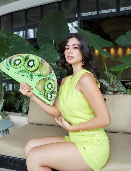 Una mujer con un vestido amarillo está parada junto a un árbol.